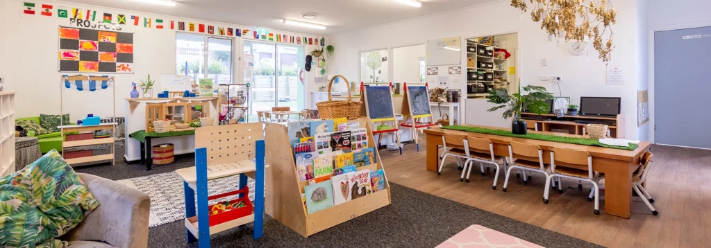 A well-organized classroom with colorful decorations, tables, chairs, bookshelves, a computer desk, and various educational materials on display.