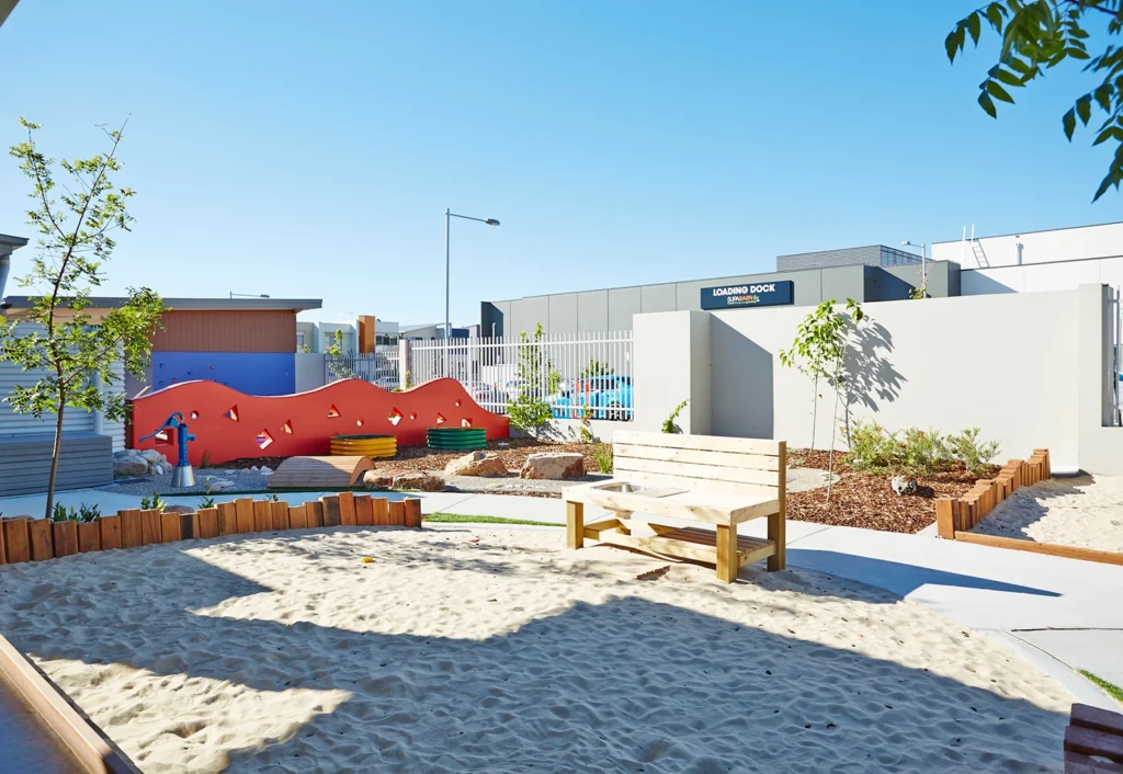 outdoor playground with sandpit and garden beds at Crace childcare