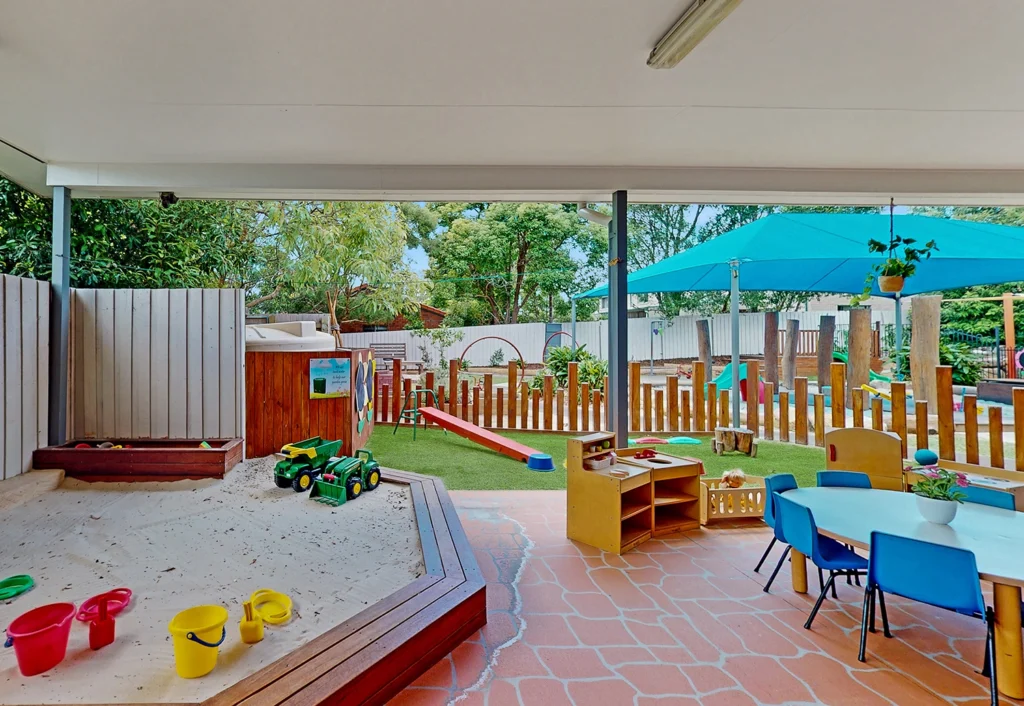 Outdoor play area for young children at Underwood childcare with a sandpit, table and chairs, surrounded by wooden fencing that allows interacting with children in the bigger kids playground.