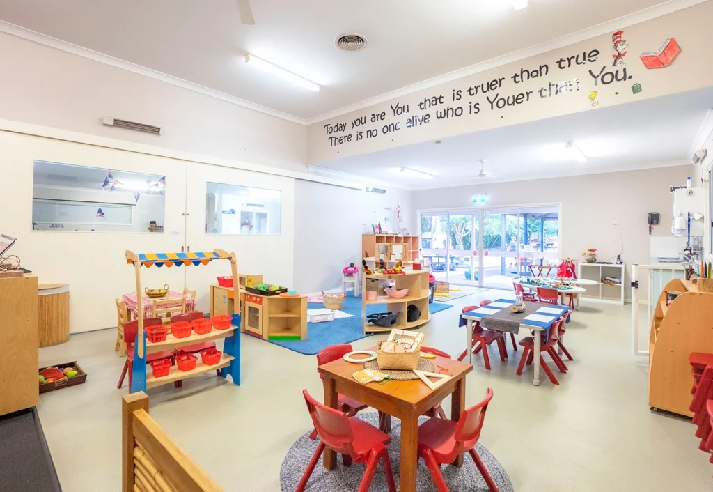 A brightly lit classroom at Fountaindale Preschool boasts various play and learning areas, including a pretend play kitchen and shop. A quote is displayed on the wall adding inspirational charm.