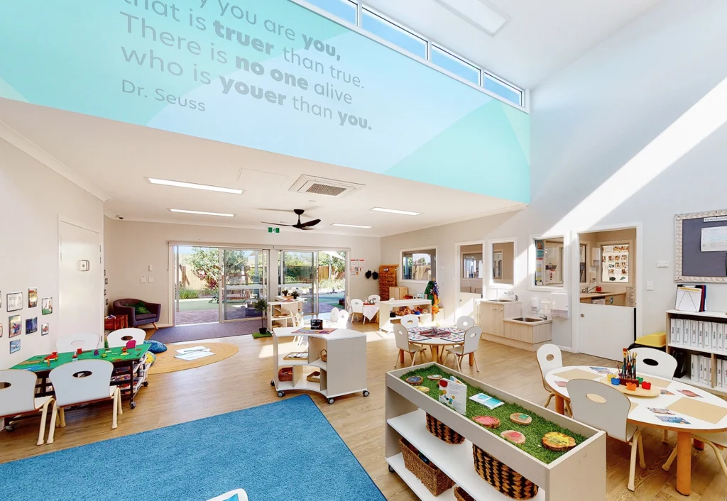 Bright and spacious classroom at Bellmere Day Care with high ceilings with tables, chairs, and educational materials.