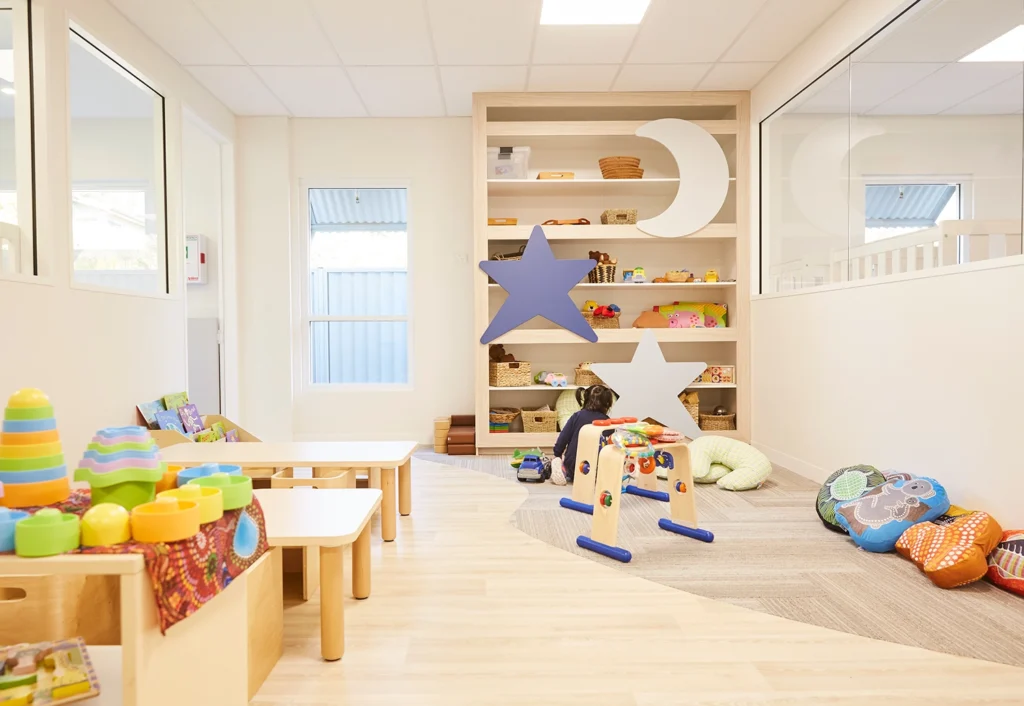 A well-lit and organized children's playroom with colorful toys, a wooden shelf with star and moon shapes, and soft seating areas.