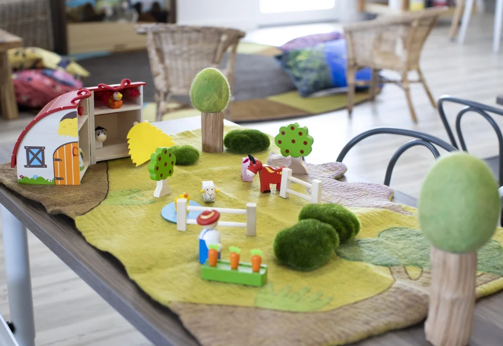 Toy farm setup on a table with a barn, trees, animals, and figures in a classroom.