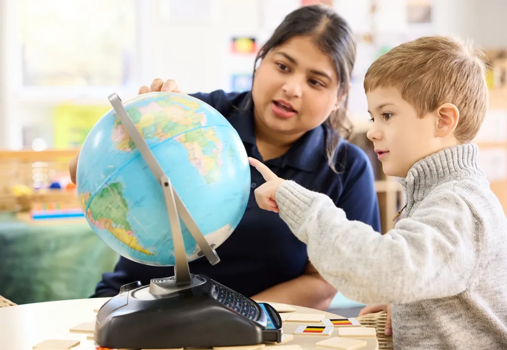 An Busy Bees educator and kindergarten boy pointing at a globe.