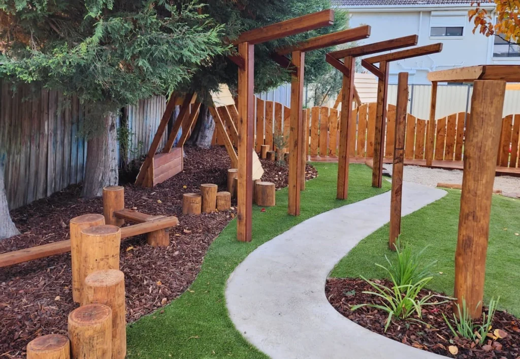 An outdoor playground at Epping Childcare with balance logs, a pathway, and water misters.