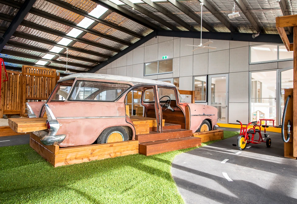 Shepparton early learning centre's indoor play area, featuring a car with wooden seating and a mock interior for role play positioned next to a bike track made to look like a road.