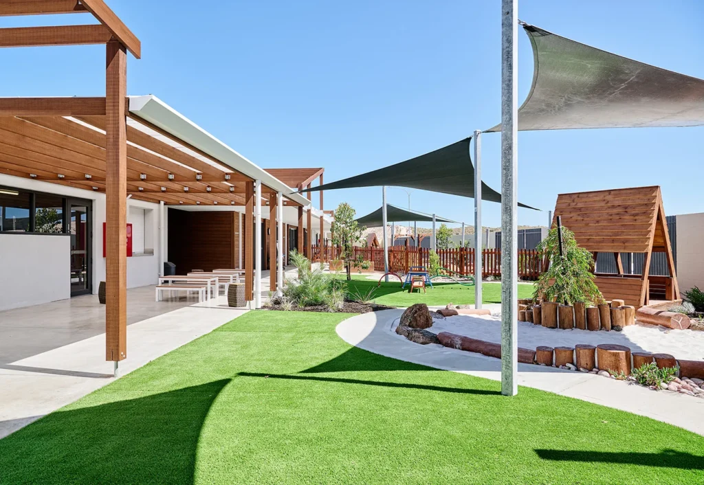 Outdoor playground at Alkimos daycare with plenty of grassy areas, shade sails, sandpit and wooden tepee.