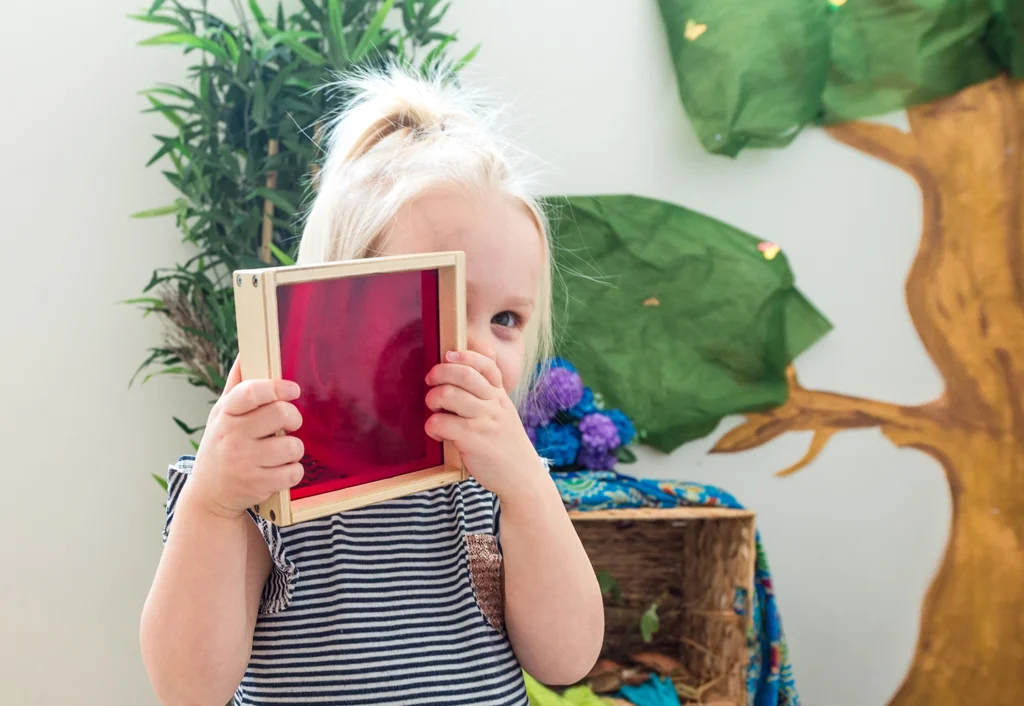 A little girl holds up a red frame, showcasing her creativity in a childcare setting.