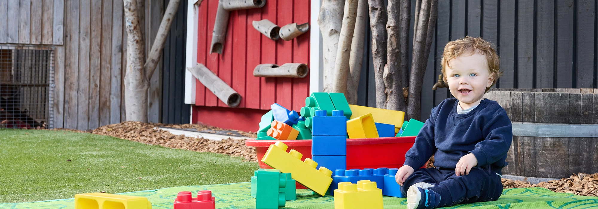 Toddler boy sitting on mat with colourful building blocks at childcare centre in Geelong West.