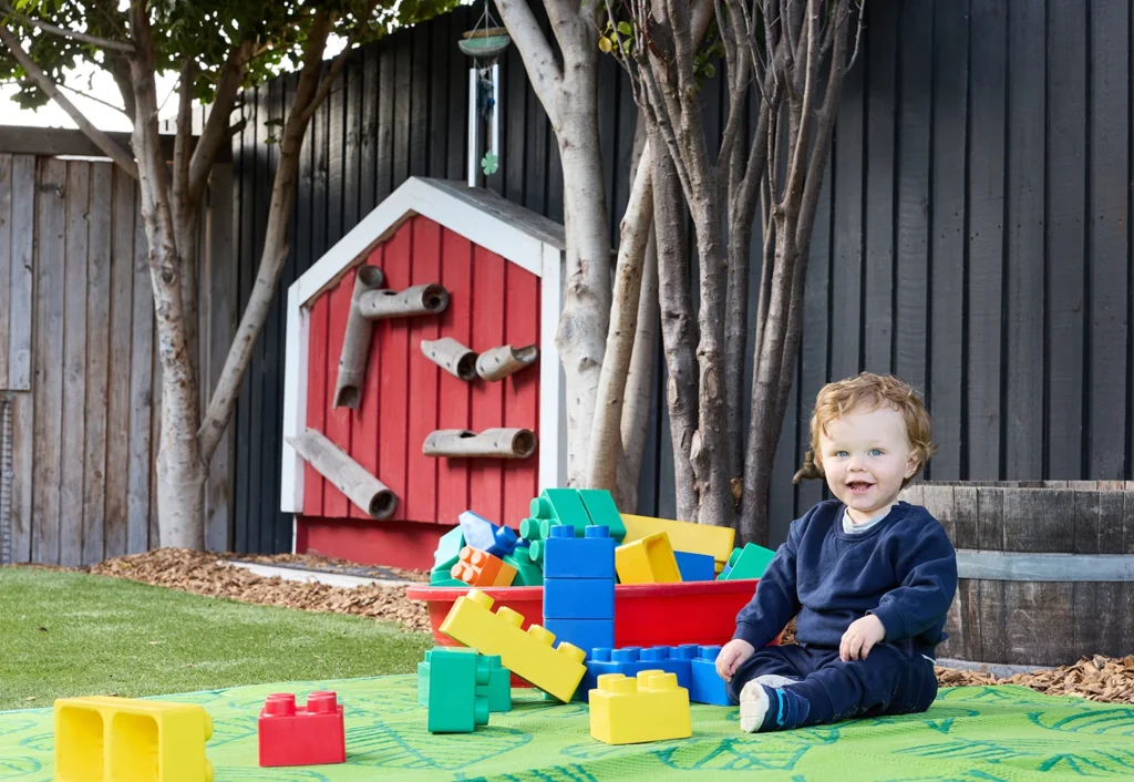 Toddler boy sitting on mat with colourful building blocks at Geelong Childcare centre.