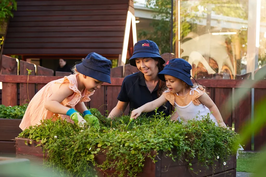 Educators with kindergarten children doing gardening