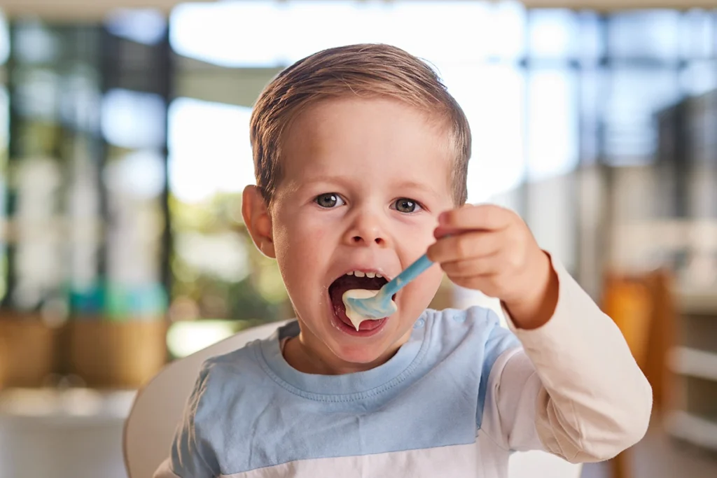 Toddler boy holding a spoonful of food to his mouth