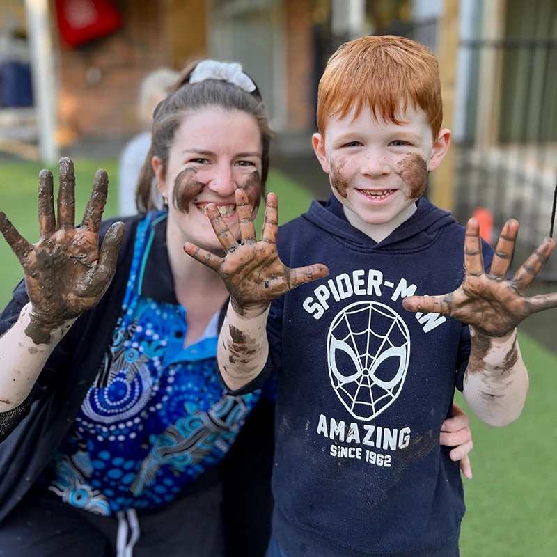 Educator and child with mud on their hands from messy play