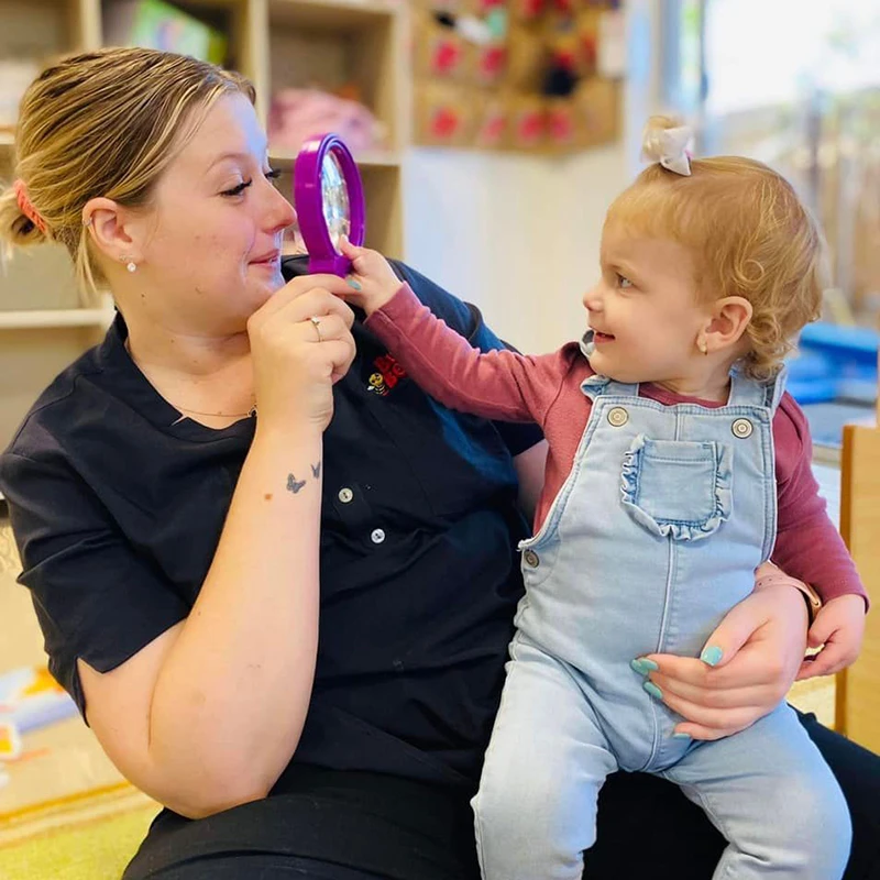 Early Childhood Educator holding young girl and magnifying glass