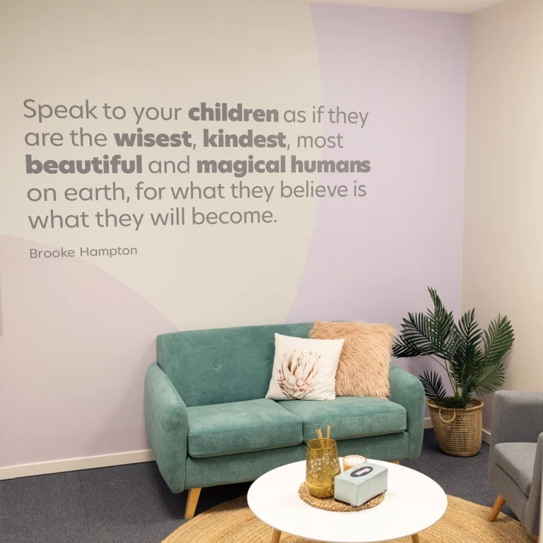 A room with pastel-colored walls features a quote on the wall, a turquoise couch with pillows, a round white coffee table with decor, and a potted plant in the corner, creating an inviting space perfect for preschool storytelling sessions.