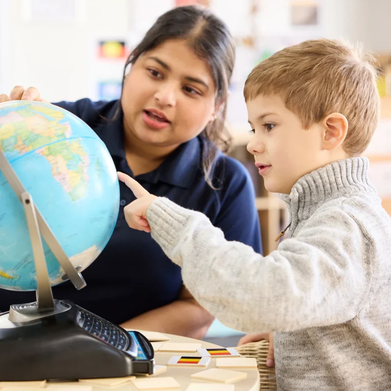 A teacher and a young student point at a globe in a kindergarten classroom, fostering early learning.