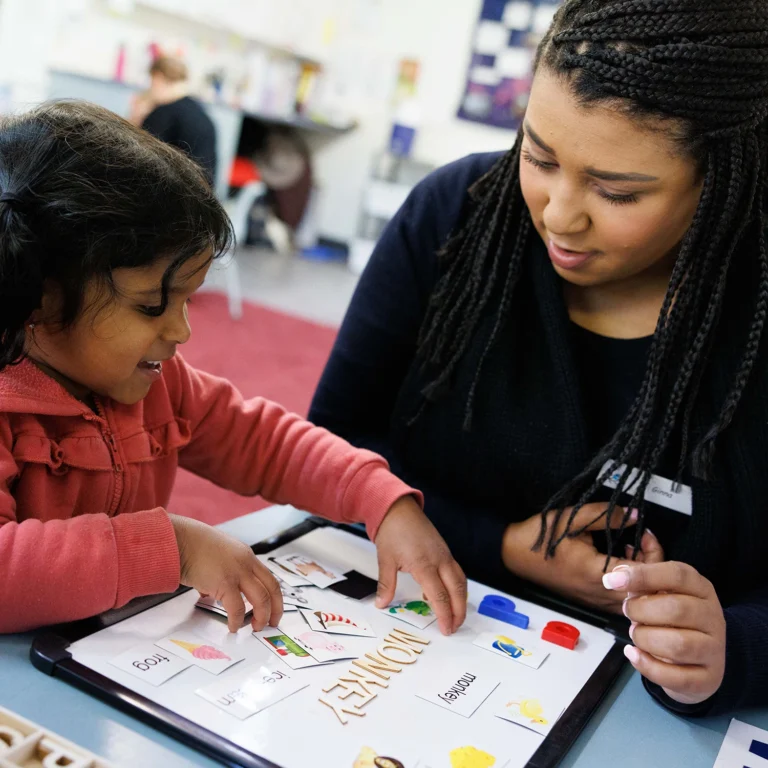 A young child and an adult interact over an educational book, with the adult fostering early learning and guiding the child's progress.