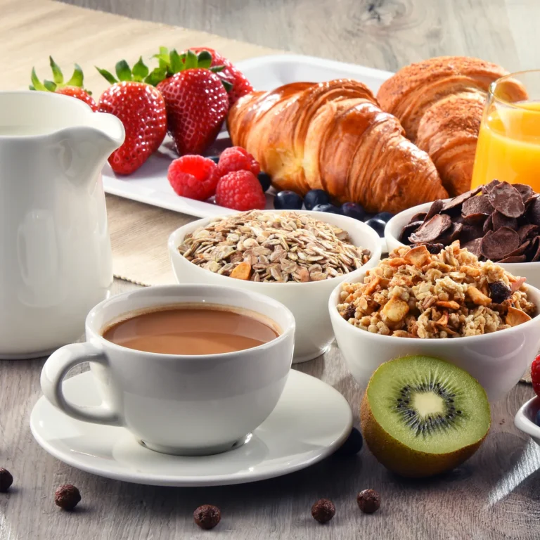 A breakfast spread with coffee, croissants, orange juice, strawberries, raspberries, mixed cereal, muesli, granola, and a half kiwi on a wooden table—a perfect treat for the daycare families.