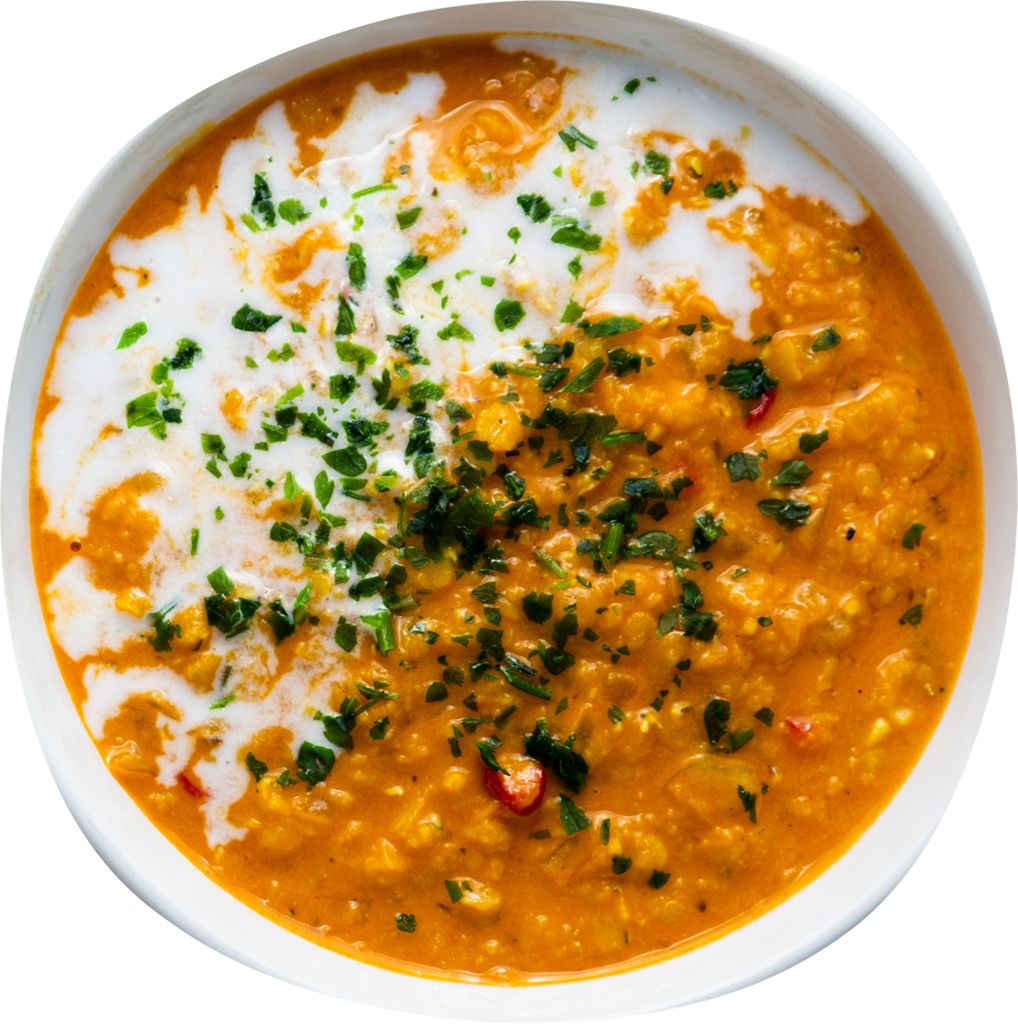 A bowl of creamy Dahl garnished with a swirl of cream and chopped herbs.