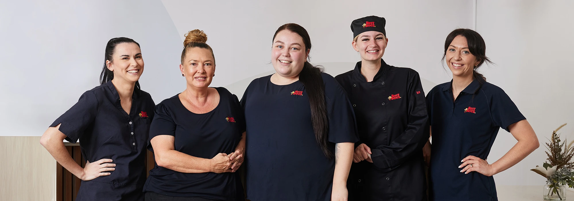 Five women in navy blue uniforms with embroidered "Busy Bees" logo.